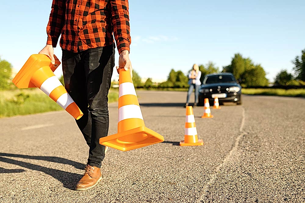 Male instructor puts traffic cones on road, driving school. Man teaching lady to drive vehicle. Driver's license education